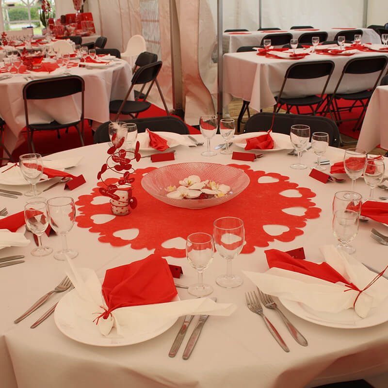 Intérieur d’une tente avec des tables hautes et des chaises recouvertes de housses blanches.